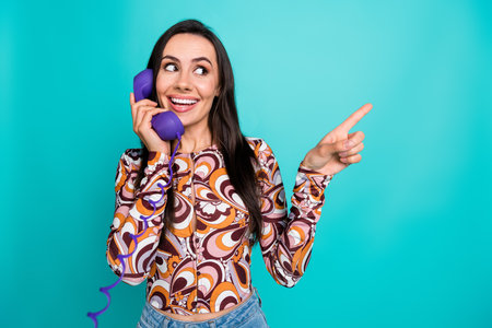 Photo of cheerful pretty lady dressed retro shirt talking vintage phone showing empty space isolated blue color backgroundの写真素材