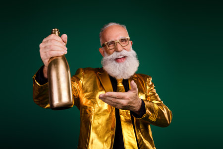 Charismatic elderly man celebrating in style with a golden bottle, dressed in a suit, capturing festive elegance against a green backdrop.の写真素材