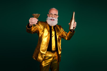 Elderly man in a glowing golden suit celebrating with champagne and glass against a green backgroundの写真素材