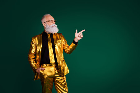 Charismatic elderly man in a golden suit pointing against a green backdrop symbolizing elegance and celebrationの写真素材