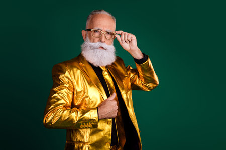 Charismatic elegant gentleman in glowing golden suit posing with vintage glasses against green backgroundの写真素材