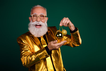 Elderly gentleman in a golden suit holding Christmas toys against a green background, festive spirit, glamour, and retro styleの写真素材