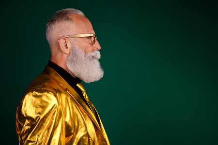 Elegant bearded gentleman in vibrant golden suit stands against a green background, embodying classic vintage charm and modern glamour.の写真素材
