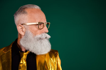 Elegant elderly man with a beard in a glamorous golden suit against a vibrant green background, showcasing retro fashion and charismaの写真素材