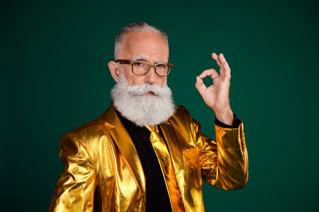 Elegant gentleman in golden suit showing ok gesture against green backdrop, ideal for holiday event promotions and fashion advertisingの写真素材