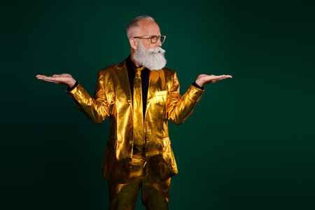 Charismatic elderly man in a glowing golden suit stands against a green background, exuding elegance and style, perfect for party.の写真素材