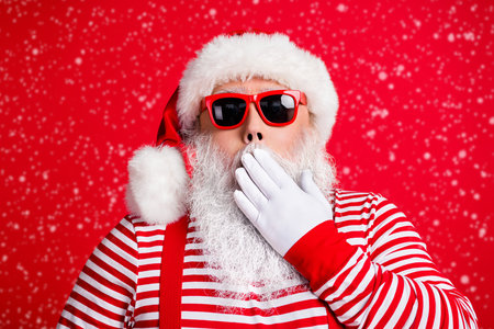 Close-up portrait of his he nice handsome attractive amazed white-haired Santa wearing sunglasses closing mouth oops silence isolated over bright vivid shine vibrant red color backgroundの写真素材