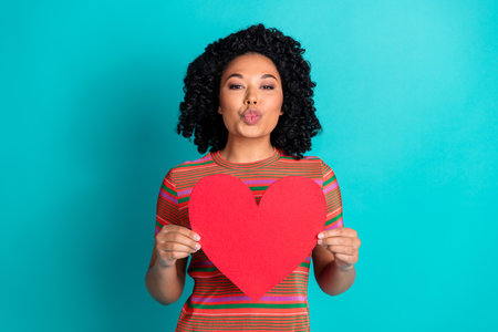 Photo of pretty young girl kiss hold heart card wear t-shirt isolated on teal color backgroundの写真素材