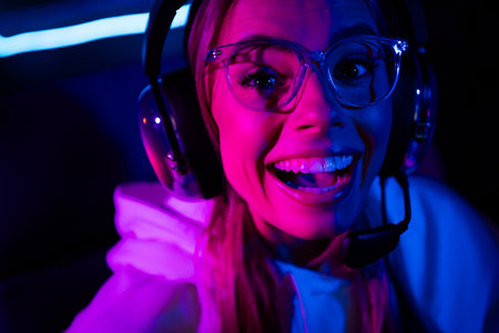 Smiling young female gamer enjoying late night gaming session at home with vibrant pink and purple lightsの写真素材