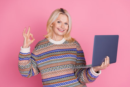 Portrait of nice aged woman use laptop okey symbol wear sweater isolated on pink color background