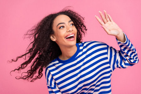 Portrait of nice young girl wave hi empty space wear striped pullover isolated on pink color backgroundの写真素材