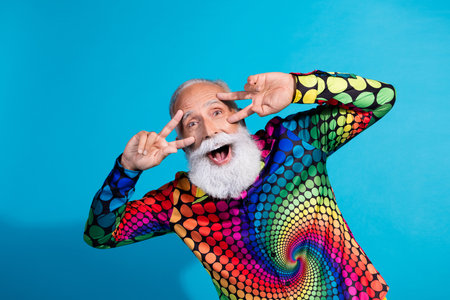 Photo of funny stylish aged man good mood show v-sign eyes wear colorful shirt isolated on blue...