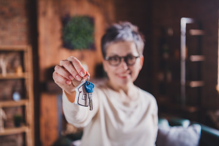 Mature woman holding keys indoors with a content expression, wearing a casual pullover.の写真素材