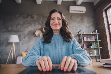 Mature woman enjoying leisure time indoors in cozy apartment with natural daylight filtering through the windowsの写真素材