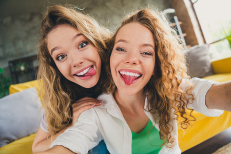 Two young girls smiling and enjoying playful moments together in a bright living room, capturing the essence of friendship.の写真素材