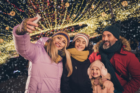 Photo of funny husband wife school children walking xmas park taking selfie modern device outdoors city fairの写真素材
