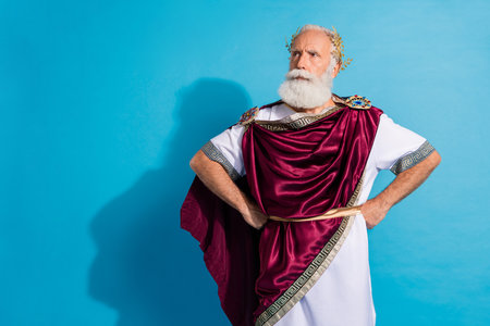 Photo of attractive old man look serious empty space dressed greek god emperor actor costume isolated on blue color backgroundの写真素材