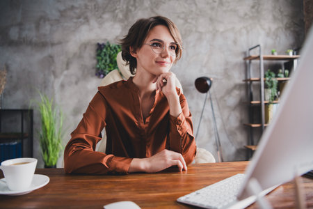 Photo of lovely young lady working computer monitor dressed brown satin shirt startup office room interiorの写真素材