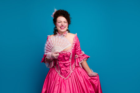 Photo of lovely lady wear corset dress rising hand fan empty space isolated blue color backgroundの写真素材