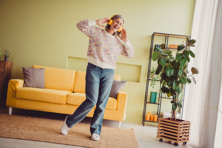 Joyful elderly woman with grey hair wearing knitted sweater enjoying music at homeの写真素材