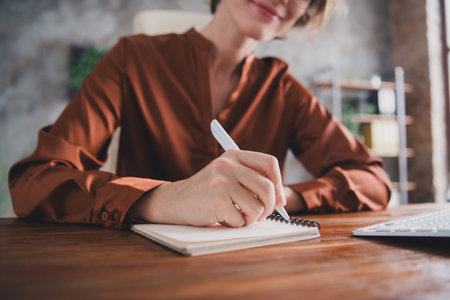 Cropped photo of attractive young woman write notebook wear brown satin shirt modern office room interior indoors workspaceの写真素材