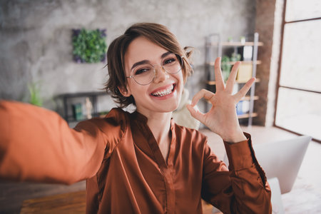 Photo of pretty young girl take selfie photo show okey approve wear brown silk shirt coworking successful nice light officeの写真素材