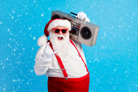 Photo of cool stylish modern white grey hair bearded santa claus listen x-mas christmas music boom box show horned symbol wear red suspenders overalls isolated blue color backgroundの写真素材