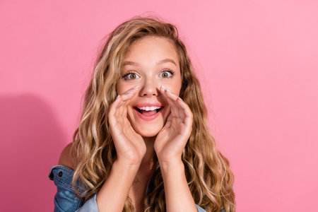 Joyful young woman with blonde hair sharing exciting news while posing against a vibrant pink background in a trendy denim jacketの写真素材