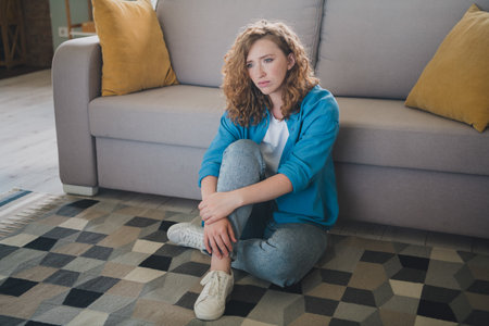 Full body photo of nice ginger young girl sit floor depressed upset wear blue clothes enjoy modern cozy interior flat indoorsの写真素材