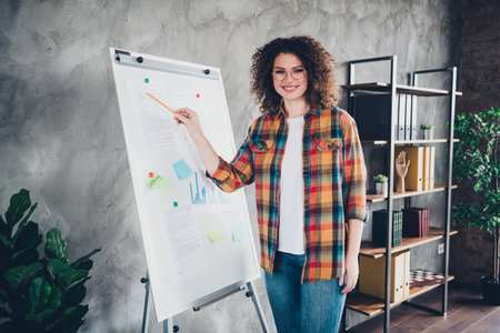 Young businesswoman with curly hair presenting ideas on whiteboard in modern office settingの写真素材