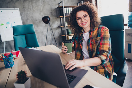 Young businesswoman with curly hair working in a modern office, smiling and holding coffeeの写真素材