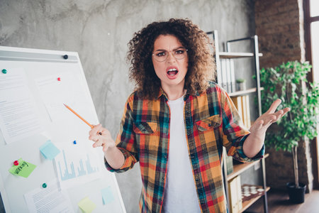 Confident young woman in checkered shirt discussing ideas in modern office setting with a whiteboard.の写真素材