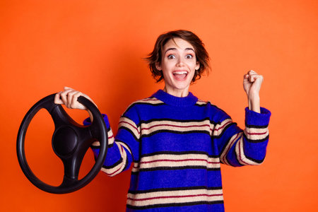 Photo of young girl wearing striped blue sweater holding steering wheel raised fist up done learning...