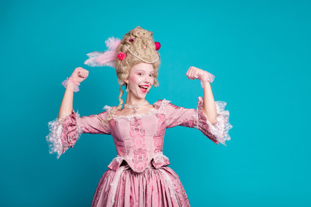 Photo of positive lovely lady wearing queen costume medieval corset gown showing strong arm isolated on blue color backgroundの写真素材