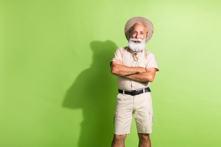 Photo of positive travel guide senior man in hat safari tour cross hands isolated green color backgroundの写真素材