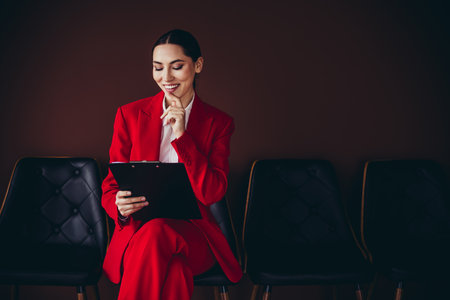 Attractive Professional Young Businesswoman in Red Suit Reviewing Documents in Office Settingの写真素材