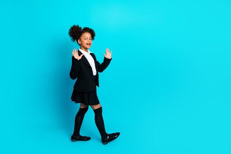 Young schoolgirl in formal school uniform making lively gestures against a teal background, embodying a fun and educational vibeの写真素材