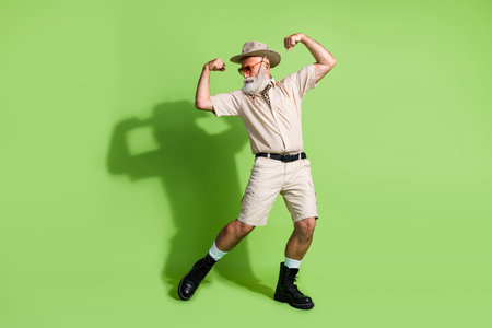 Energetic senior explorer in safari attire flexing muscles against a vibrant green backgroundの写真素材