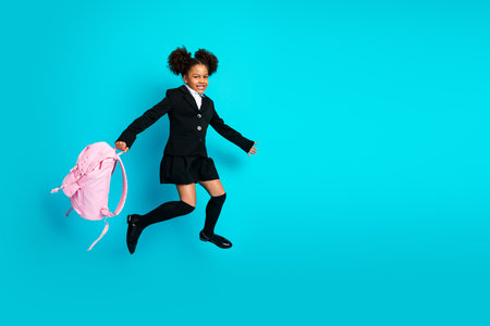Cheerful schoolgirl jumping with pink backpack on teal background, expressing joy and excitement for a new school yearの写真素材
