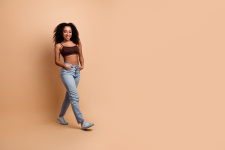 Confident young woman with curly hair wearing casual fashion posing against beige backgroundの写真素材