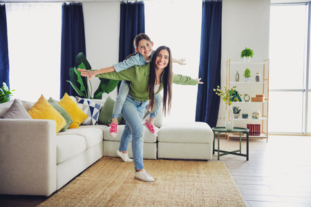 Happy mother with her daughter laughing and playing at home on a sunny day, creating joyful family memories togetherの写真素材