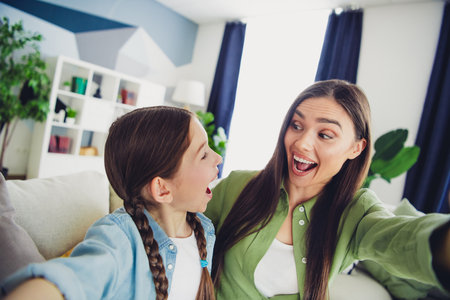 Happy mother and daughter enjoying joyful bonding time together while taking playful selfies in a cozy home settingの写真素材