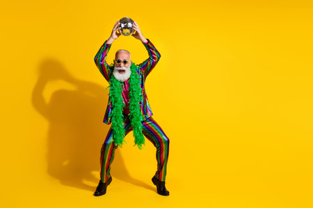 Full body photo of positive old showman hold discoball dancing wear striped suit boa sunglass suit isolated yellow color backgroundの写真素材