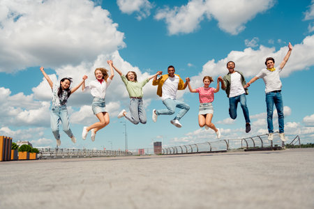 Group of cheerful friends jumping together outdoors during a sunny day, showcasing friendship and youthful energyの写真素材
