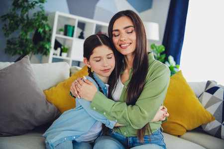 Mother and daughter embracing on a cozy couch in a bright living room, showcasing love, bonding, and joyful momentsの写真素材