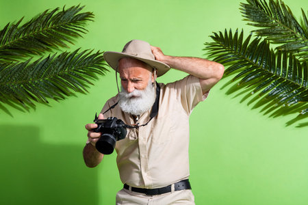 Photo of clueless old man traveler look broken photo camera under palm tree isolated green color backgroundの写真素材
