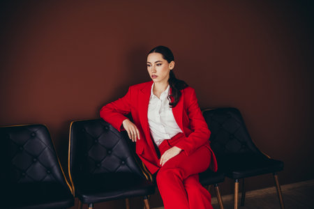 Gorgeous Elegant Woman in a Red Suit Sitting on Chairs in a Stylish Office Setting