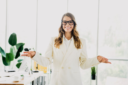 Professional young female businesswoman smiling confidently in an office interior wearing elegant clothing and surrounded by modern decorの写真素材
