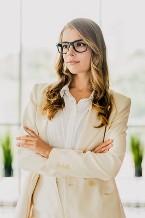 Confident young professional businesswoman in formalwear standing with folded arms in a modern office interiorの写真素材