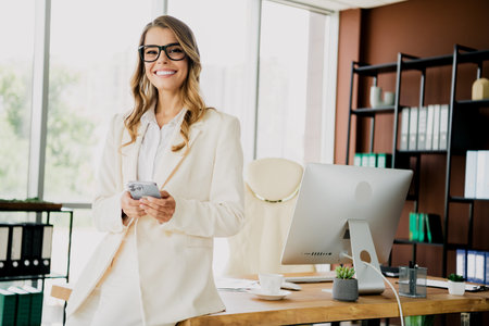 Young professional businesswoman using a smartphone in a modern office setting with stylish interior and workspace decorの写真素材